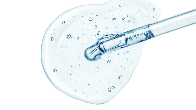 A pipette dispensing a liquid onto a white surface, with bubbles forming in the liquid.