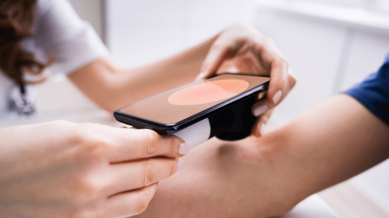 Человек держит смартфон с размытым экраном, в нижней части которого виден сканер отпечатков пальцев. Телефон находится в вертикальном положении.