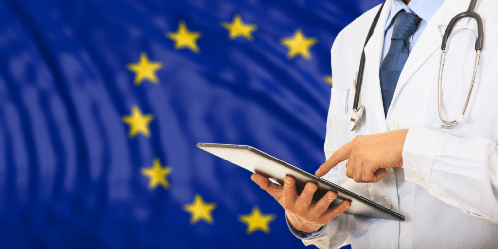 Un médico sostiene una tableta con la bandera de la Unión Europea al fondo.