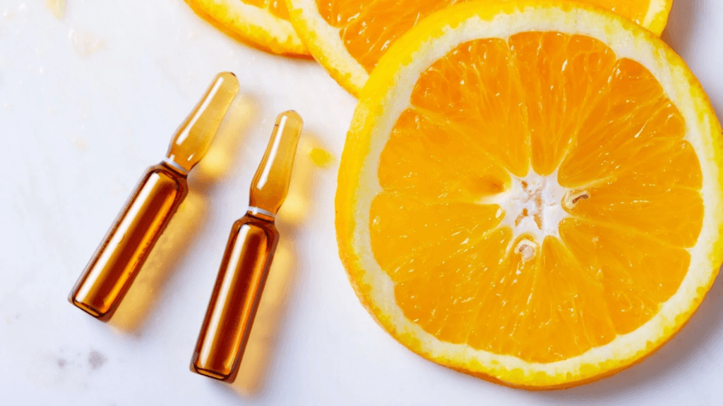 Dos pequeños frascos de color naranja junto a varias rodajas de naranja fresca sobre una superficie blanca.