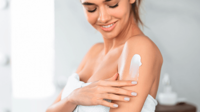 A woman applying cream to her arm while smiling.